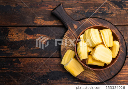 Sweet, golden jackfruit pods (bulbs) in a wooden bowl on a rustic dark wood table. Tropical fruit snack with copy space. Sweet, golden jackfruit pods (bulbs) in a wooden bowl on a rustic dark wood table. Tropical fruit snack with copy space. 133324026