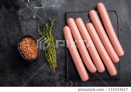 Four raw pink hot dog sausages (frankfurters/wieners) on a contrasting dark stone background with Himalayan salt. Copy space. 133324027