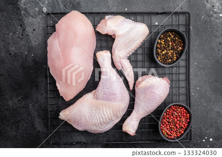 Assortment of fresh raw chicken meat on a metal rack over a textured black surface. High angle view with generous copy space. Assortment of fresh raw chicken meat on a metal rack over a textured black surface. High angle view with generous copy space. 133324030