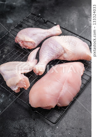 Assortment of fresh raw chicken meat on a metal rack over a textured black surface. High angle view with generous copy space. 133324033