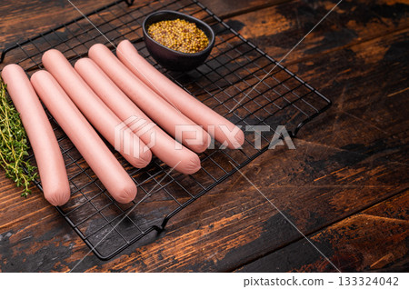 Top-down view of uncooked frankfurters ready for the grill, with herbs and mustard on a dark, rustic wood background. Top-down view of uncooked frankfurters ready for the grill, with herbs and mustard on a dark, rustic wood background. 133324042