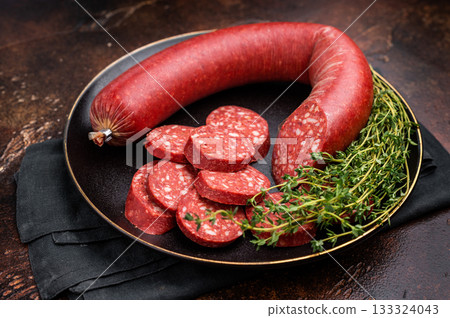 Sliced and whole Turkish sucuk (sujuk) in a cast iron pan with thyme. Spicy dry-cured sausage, top view. 133324043