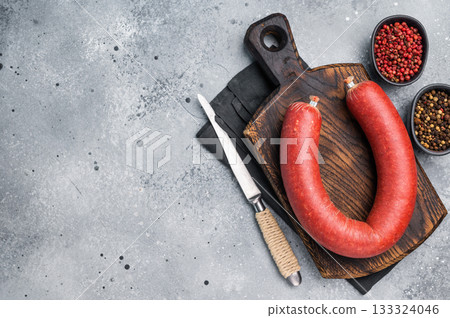 Raw Turkish sucuk (sujuk) on a cutting board with a knife and spices. Traditional spicy dry-cured sausage, top view. 133324046