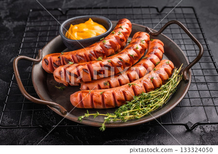 Grilled and cut sausages (frankfurters/wieners) on a rustic platter with mustard sauce and thyme on a dark textured background. Grilled and cut sausages (frankfurters/wieners) on a rustic platter with mustard sauce and thyme on a dark textured background. 133324050