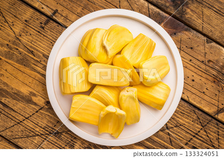 Sweet, golden yellow jackfruit pods (bulbs) served on a white plate on a rustic wooden table. Fresh, tropical fruit snack. 133324051