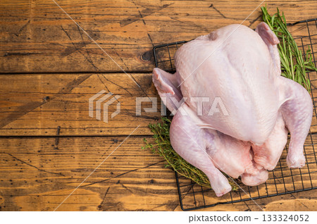 Whole fresh raw chicken on a cooling rack with rosemary and thyme. Ready for cooking on a rustic wooden table. Whole fresh raw chicken on a cooling rack with rosemary and thyme. Ready for cooking on a rustic wooden table. 133324052