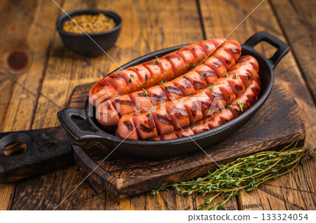 Juicy, smoky fried sausages on a wooden board with herbs and fork. High-quality image for restaurant menus or food blog headers. 133324054