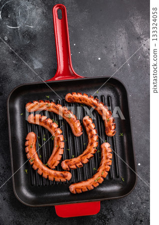Grilled and cut sausages (wieners/frankfurters) in a hot cast iron grill pan on a dark background. Ready meal concept for dinner or BBQ. Grilled and cut sausages (wieners/frankfurters) in a hot cast iron grill pan on a dark background. Ready meal concept for dinner or BBQ. 133324058