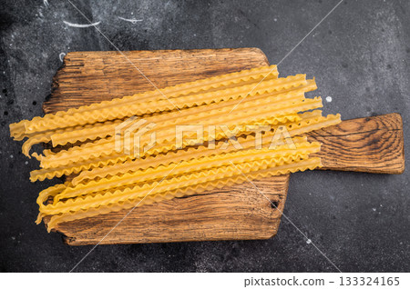 Uncooked mafaldine, ready to be transformed into a delicious dish that highlights its delightful texture. black background. top view Uncooked mafaldine, ready to be transformed into a delicious dish that highlights its delightful texture. black background. top view 133324165
