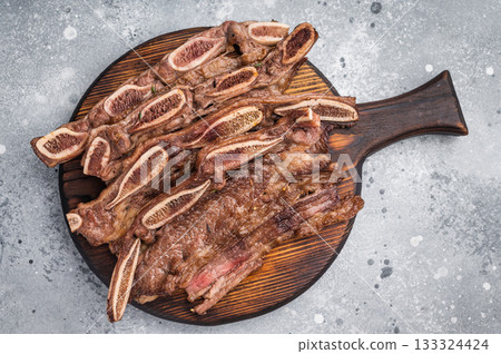 Appetizing roasted beef short ribs with bone and Himalayan salt. Gourmet presentation with herbs on a stone table. Appetizing roasted beef short ribs with bone and Himalayan salt. Gourmet presentation with herbs on a stone table. 133324424