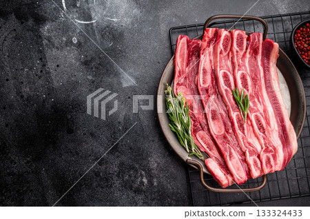 Raw Flanken cut beef short ribs (Kalbi) with rosemary and thyme on a dark, rustic background. Copy space. Raw Flanken cut beef short ribs (Kalbi) with rosemary and thyme on a dark, rustic background. Copy space. 133324433