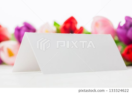 Flat minimal design blank tent-style card is standing on white surface with blurred tulip backdrop Flat minimal design blank tent-style card is standing on white surface with blurred tulip backdrop 133324622