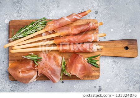 Gourmet Italian Antipasto with prosciutto crudo, grissini breadsticks, and olives on a rustic wooden board. Top view with copy space. 133324876