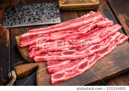 Raw Flanken cut beef short ribs and a rustic cleaver on a dark wooden background with ample copy space. 133324885