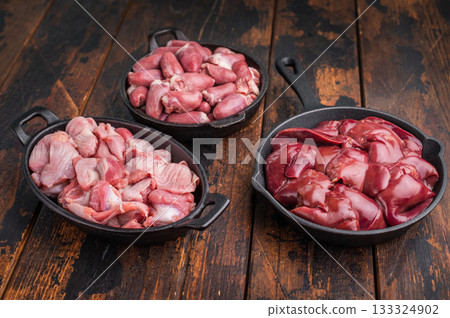 Fresh raw poultry offal assortment with duck hearts, liver, and gizzards on dark rustic wood table, organic cooking concept. 133324902