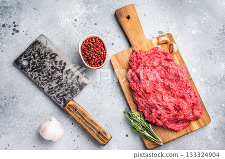 Raw ground venison (wild deer meat) with fresh rosemary and garlic on a wooden board against a modern gray stone background. 133324904