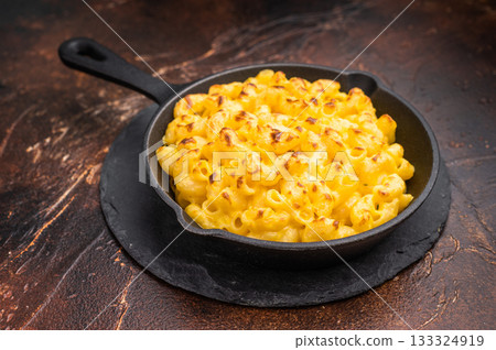 Baked mac and cheese in a black skillet, set against a rustic dark brown background 133324919