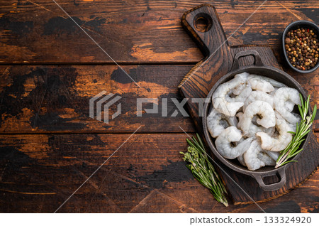 Raw peeled shrimp prawn and rosemary in a dark cast iron skillet on a rustic wooden background. Top view with copy space for recipe or menu. Raw peeled shrimp prawn and rosemary in a dark cast iron skillet on a rustic wooden background. Top view with copy space for recipe or menu. 133324920