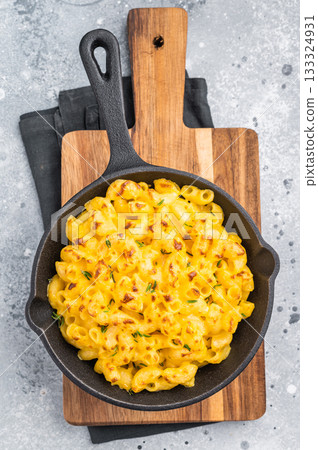 Savory baked macaroni with cheese in a skillet. Wooden board and gray surface add a cozy, stylish touch. 133324931