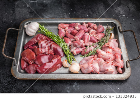 Assorted raw poultry giblets including chicken liver, gizzards, and hearts with herbs and garlic on rustic metal tray top view. Assorted raw poultry giblets including chicken liver, gizzards, and hearts with herbs and garlic on rustic metal tray top view. 133324933