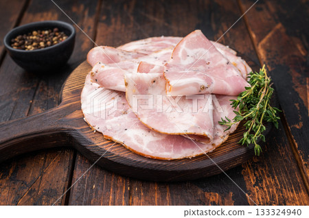 Slices of authentic Italian Pancetta Arrotolata served on a dark rustic cutting board with fresh thyme and peppercorns. Slices of authentic Italian Pancetta Arrotolata served on a dark rustic cutting board with fresh thyme and peppercorns. 133324940