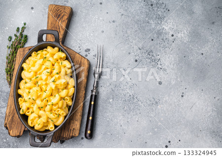 Creamy mac and cheese in a black cast iron skillet, resting on a rustic wooden board against a gray background. Creamy mac and cheese in a black cast iron skillet, resting on a rustic wooden board against a gray background. 133324945