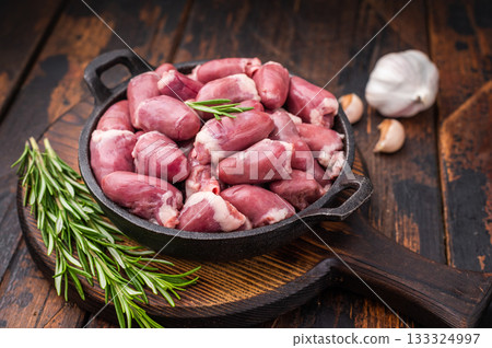 Raw chicken hearts in cast iron skillet, surrounded by garlic and rosemary on rustic wooden background 133324997