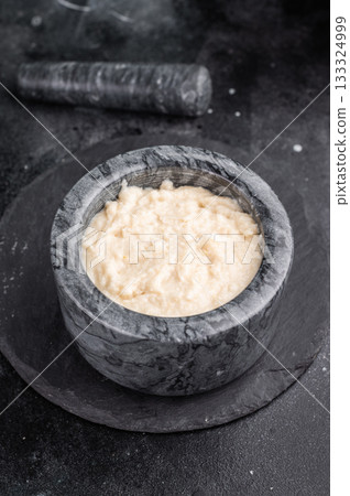Dark and moody food photo. Creamy horseradish sauce in a marble mortar and pestle, set on a textured slate background. Copy space. 133324999