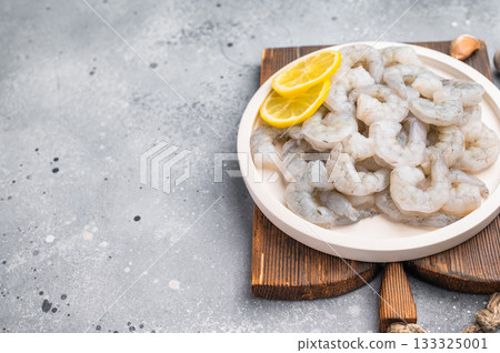Fresh prawn shrimp tails on a wooden board. Gourmet ingredient with spices and lemon slices, ready for cooking on a rustic table. 133325001