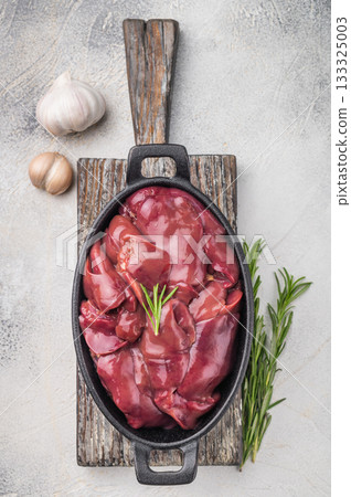 Fresh duck liver in a cast iron dish, accompanied by garlic cloves and a sprig of rosemary. The grey textured surface creates a stylish contrast. Fresh duck liver in a cast iron dish, accompanied by garlic cloves and a sprig of rosemary. The grey textured surface creates a stylish contrast. 133325003