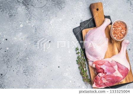 Raw duck legs on a wooden cutting board, accompanied by Himalayan salt and thyme sprig, set against a neutral gray backdrop Raw duck legs on a wooden cutting board, accompanied by Himalayan salt and thyme sprig, set against a neutral gray backdrop 133325004
