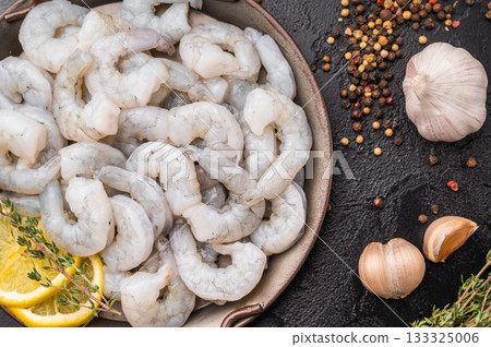 Raw peeled shrimp prawn with lemon and thyme in a metal pan on a textured black background. Maximum contrast with copy space. 133325006