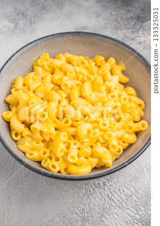 Creamy macaroni and cheese in a rustic bowl on a wooden board, set against a textured gray background 133325031