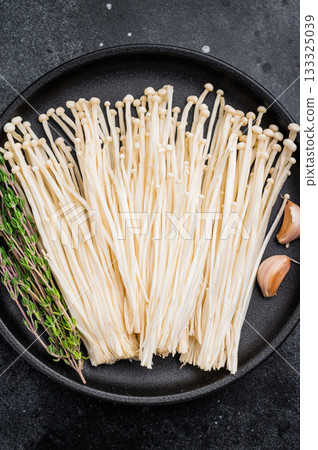 Top view of raw Enokitake on a dark textured surface. High-contrast, moody food photography for healthy cooking. Top view of raw Enokitake on a dark textured surface. High-contrast, moody food photography for healthy cooking. 133325039