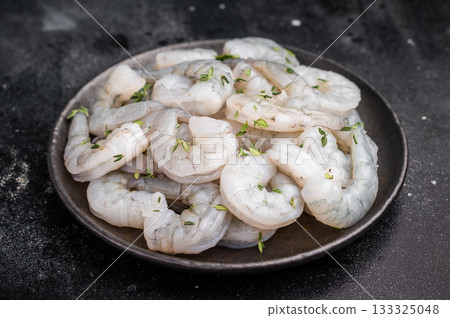 Raw peeled shrimp with thyme in a dark metal plate on a textured black background. Maximum contrast with copy space. 133325048