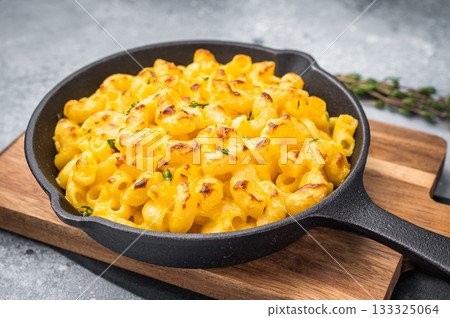 Savory baked macaroni with cheese in a skillet. Wooden board and gray surface add a cozy, stylish touch. 133325064