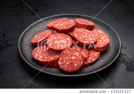 Pile of sliced Turkish sucuk (sujuk) on a dark plate. Traditional spicy dry-cured sausage, ready to eat. 133325127