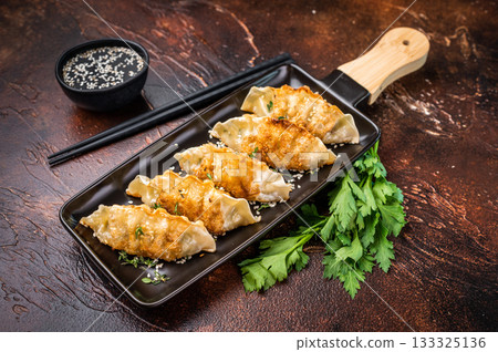 Fried Jiaozi on plate with sauce, Chinese Dumplings with shrimps and vegetables. brown background. top view 133325136