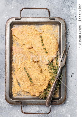 Cooking of Raw breaded Wiener Schnitzel steak in steel tray. gray background. top view 133325162