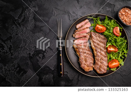 Grilled Steak from Black Angus beef meat on a plate with salad. black background. top view Grilled Steak from Black Angus beef meat on a plate with salad. black background. top view 133325163
