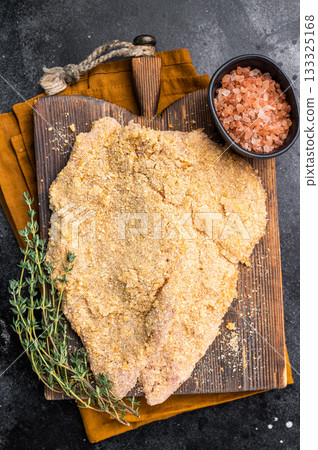 Wiener breaded raw pork Schnitzel, meat steak on a wooden board. black background. top view Wiener breaded raw pork Schnitzel, meat steak on a wooden board. black background. top view 133325168