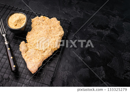 Raw breaded pork Schnitzel steak on a rack. black background. top view Raw breaded pork Schnitzel steak on a rack. black background. top view 133325279