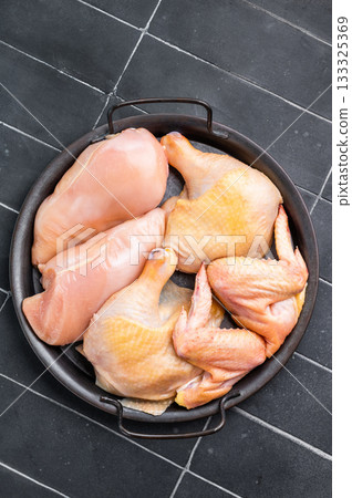 A black metal dish with a handle holds several pieces of fresh, raw chicken. The chicken is arranged neatly in the dish A black metal dish with a handle holds several pieces of fresh, raw chicken. The chicken is arranged neatly in the dish 133325369