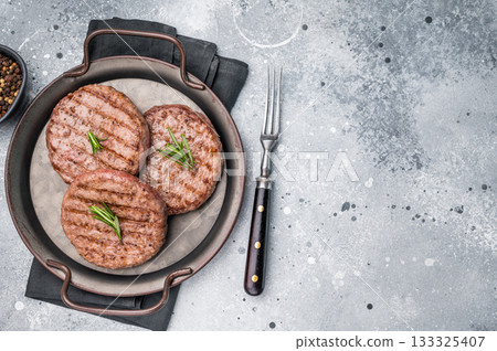 Close up of a flavorful grilled beef meat patty, ready to be topped with fresh ingredients for a delicious meal. grey background. top view Close up of a flavorful grilled beef meat patty, ready to be topped with fresh ingredients for a delicious meal. grey background. top view 133325407