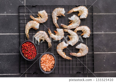 Raw shrimps, headless fresh prawns on a rack. Top view. Black background Raw shrimps, headless fresh prawns on a rack. Top view. Black background 133325410