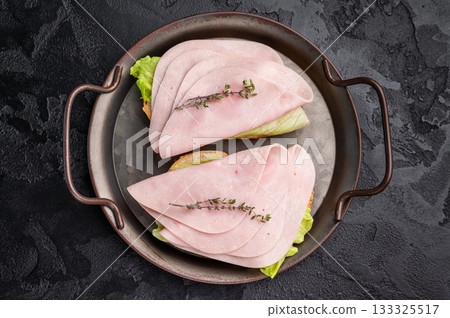 Delicious ham sandwich stacked high with fresh veggies, perfect for a quick lunch or picnic delight. black background. top view 133325517