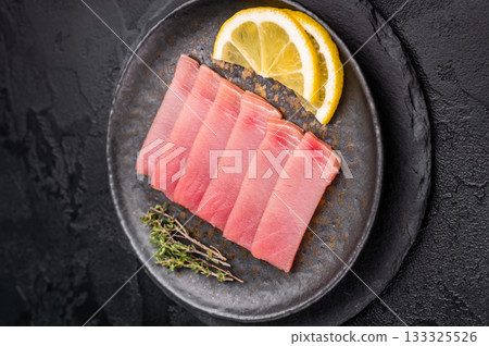 Vibrant tuna sashimi arranged on a plate, showcasing its rich color and delicate texture for an exquisite meal. black background. top view Vibrant tuna sashimi arranged on a plate, showcasing its rich color and delicate texture for an exquisite meal. black background. top view 133325526