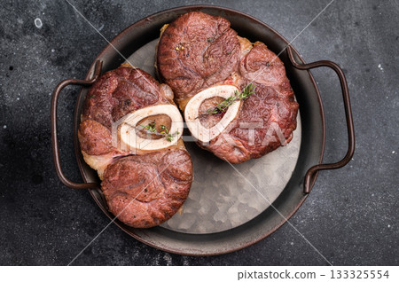 Deliciously braised ossobuco, featuring tender osso buco veal shank and rich marrow, perfect for a gourmet Italian feast. black background. top view Deliciously braised ossobuco, featuring tender osso buco veal shank and rich marrow, perfect for a gourmet Italian feast. black background. top view 133325554