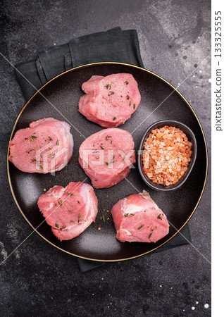 Tender fresh pork medallion, raw tenderloin meat perfect for elevating your dinner table with a touch of culinary finesse. black background. top view Tender fresh pork medallion, raw tenderloin meat perfect for elevating your dinner table with a touch of culinary finesse. black background. top view 133325555