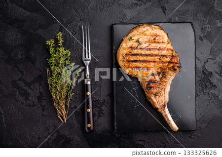 Savory bone in pork chop steak, beautifully charred and ready to impress at your next barbecue gathering. black background. top view Savory bone in pork chop steak, beautifully charred and ready to impress at your next barbecue gathering. black background. top view 133325626